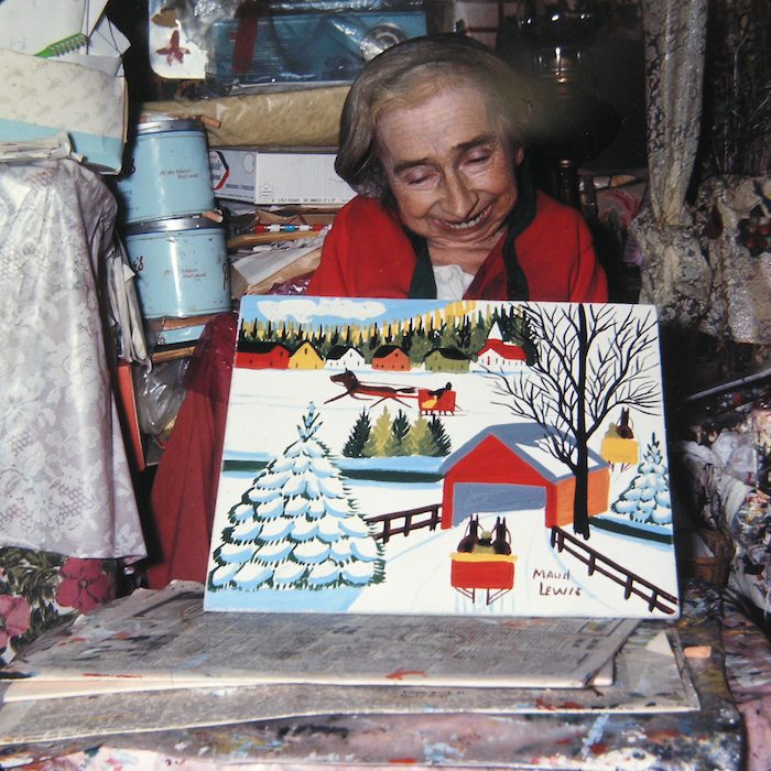 Artist Maud Lewis holds one of her paintings of a winter landscape