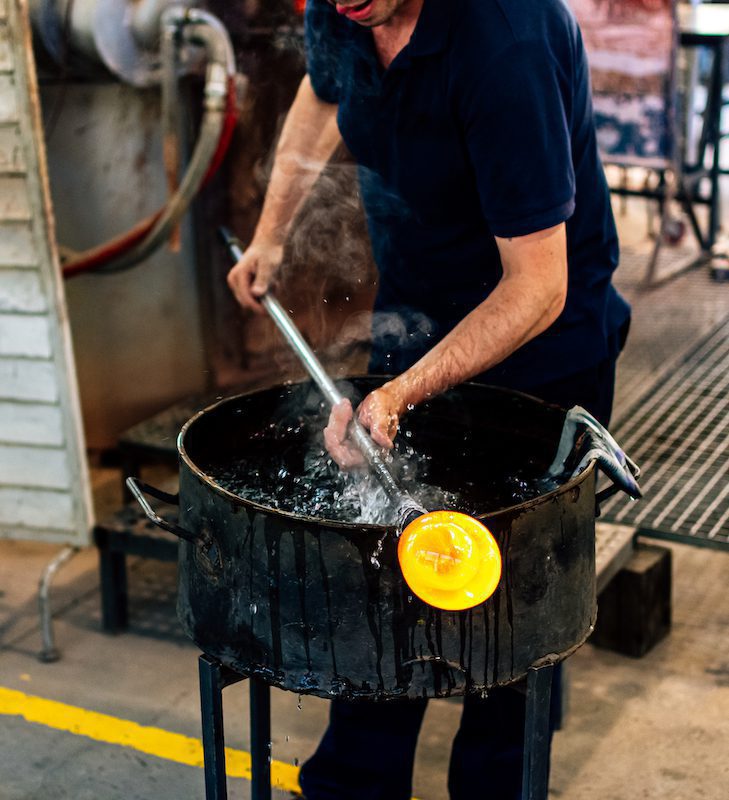 Glassworks glass manufacturing. Glass artisan working on a piece of hot glass.