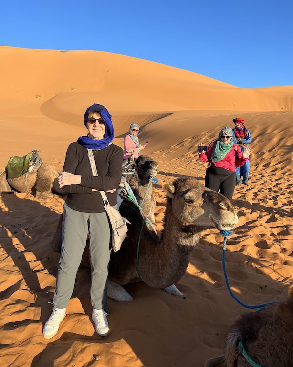 A woman stands next to a resting camel in the Sahara Desert