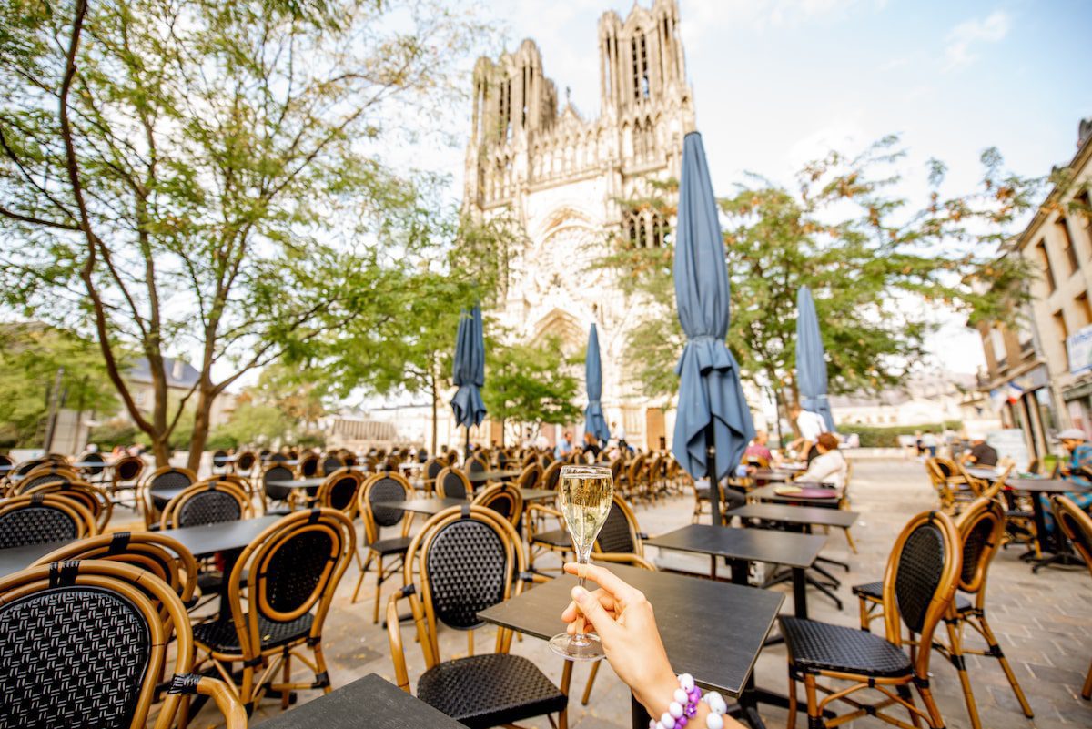 Holding a glass of champagne outdoors with Reims cathedral on the background at the capital of Champagne wine region