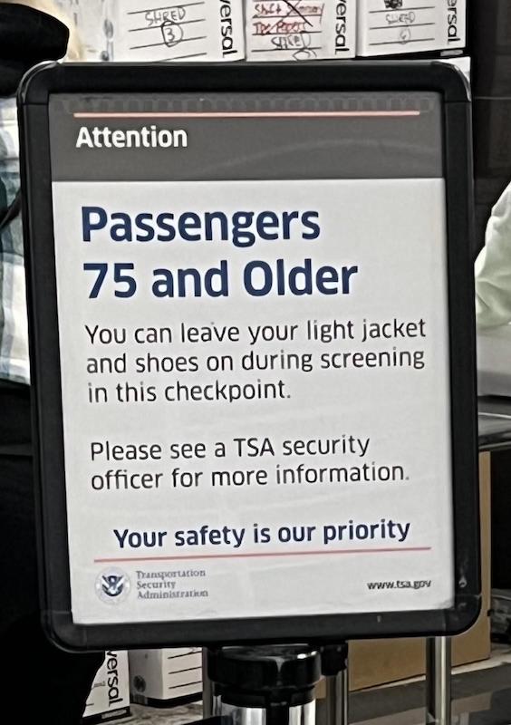 A TSA sign at an airport showing that passengers over the age of 75 don't need to remove their shoes or sweaters, in age-friendly airports