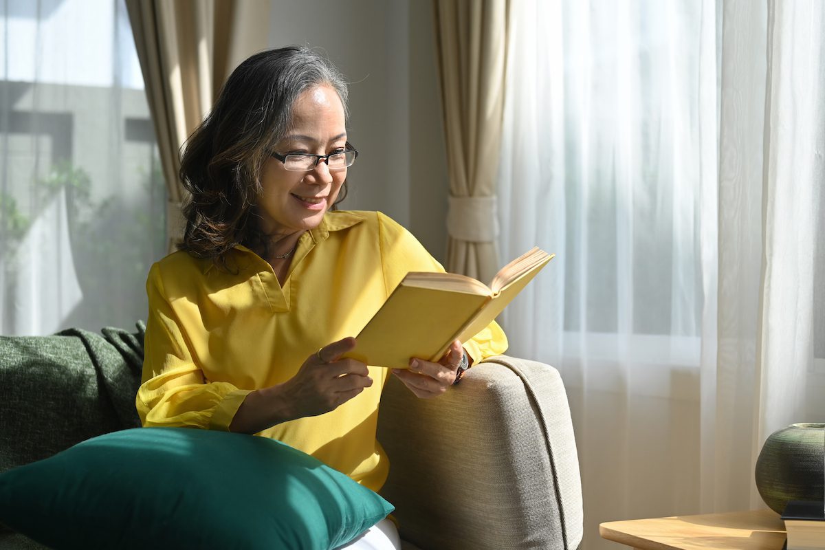 Peaceful mature woman reading book while resting on comfortable sofa a home.