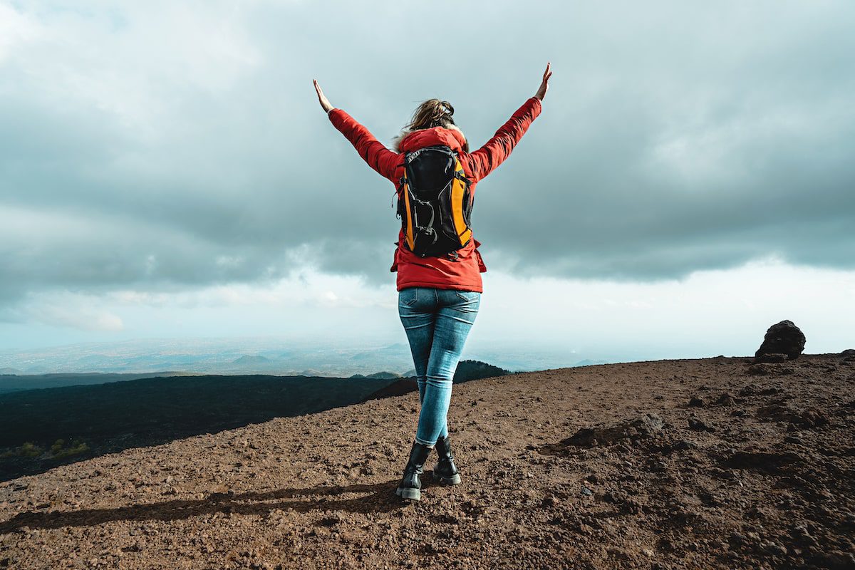 A woman woman hiker standing on the mountain peak with arms raised