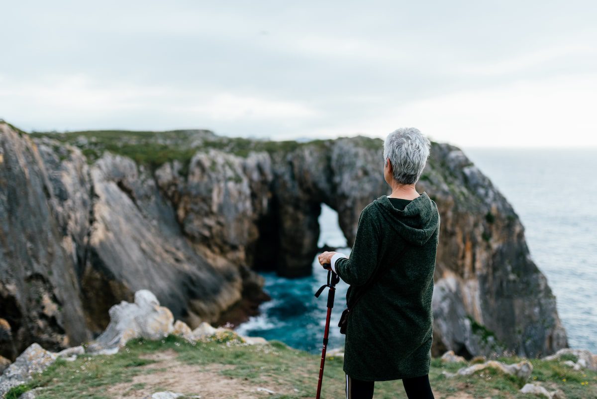 Senior woman with trekking sticks hiking next to the ocean near some cliffs