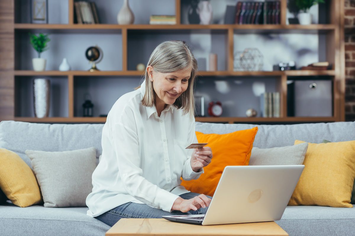 Woman sitting on the couch with a laptop holding a credit bank card, looking for airline credit card deals.