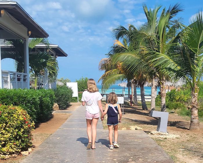 Two young girls walk down a path surrounded by palm trees