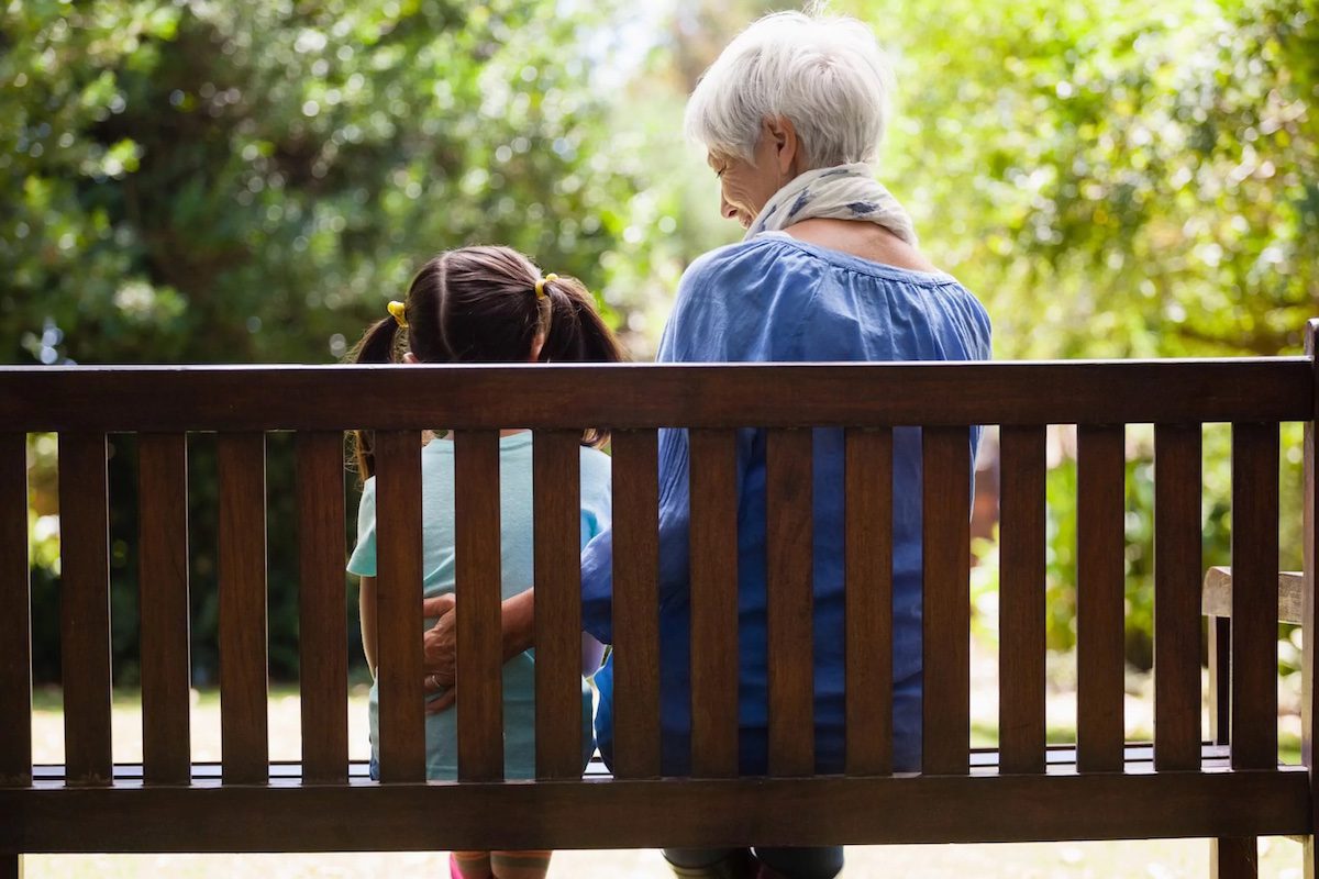 A grandmother with one of her grandchildren sitting on a bench.