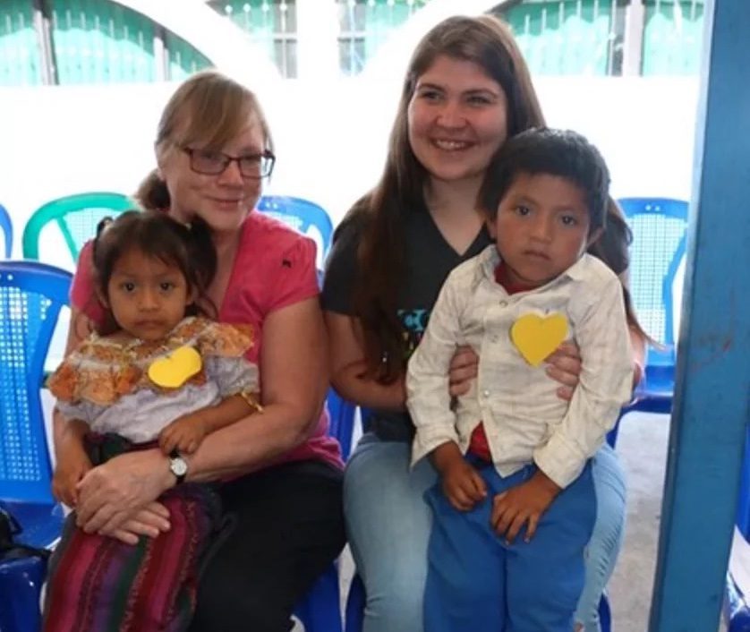 Two woman sit holding two young grandchildren