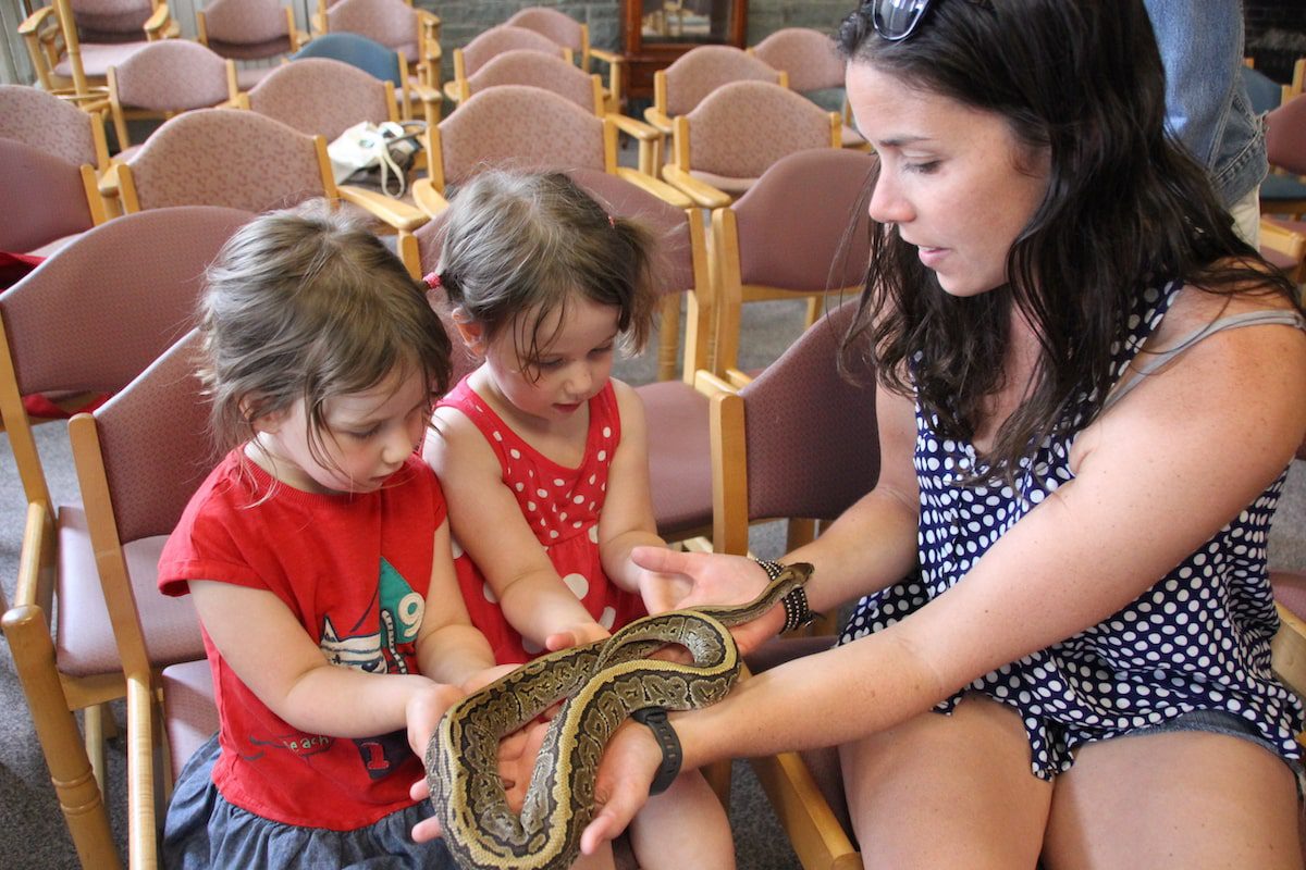 A woman and two children hold a snake in a reptile exhibit