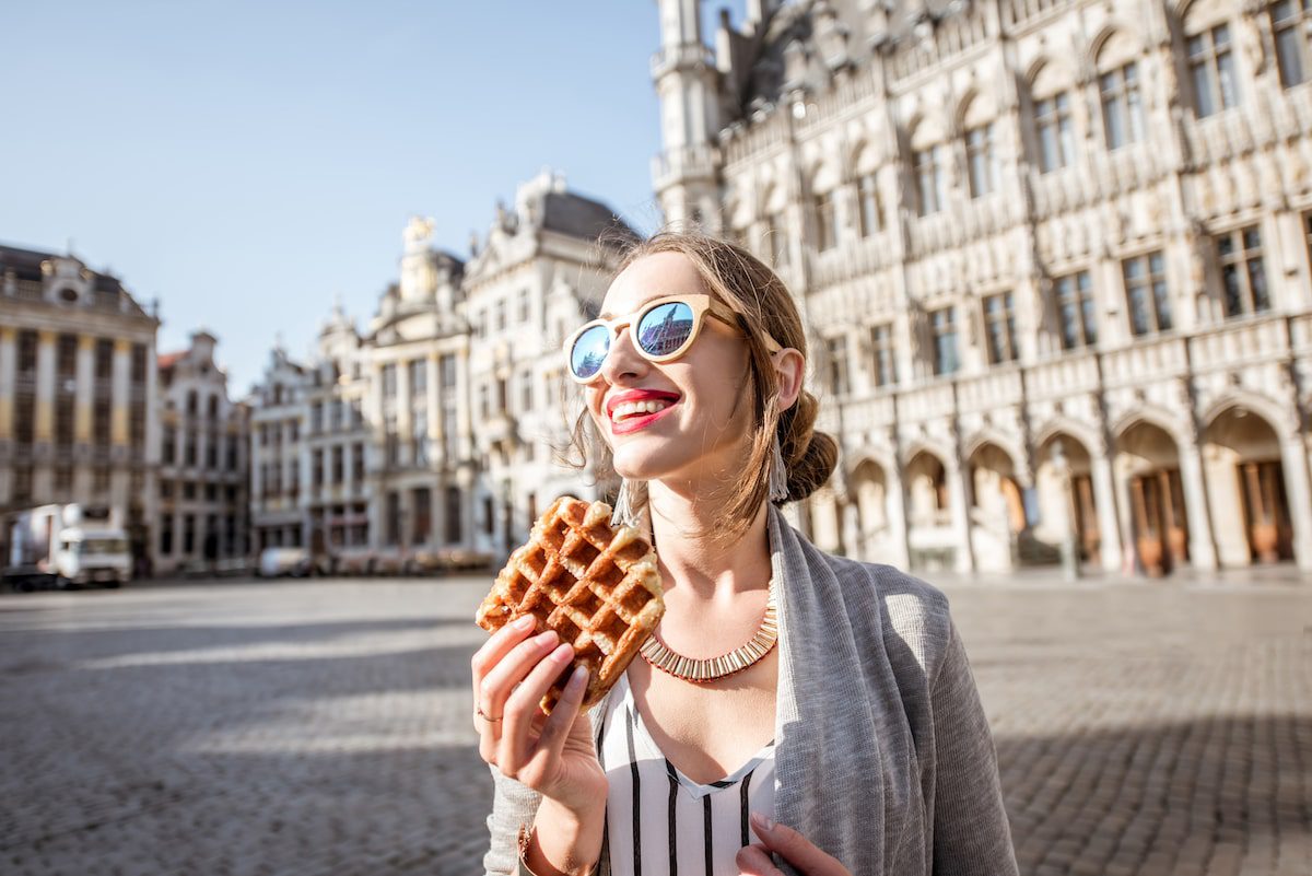A woman eats a Belgian waffle outside a historic building in Brussels