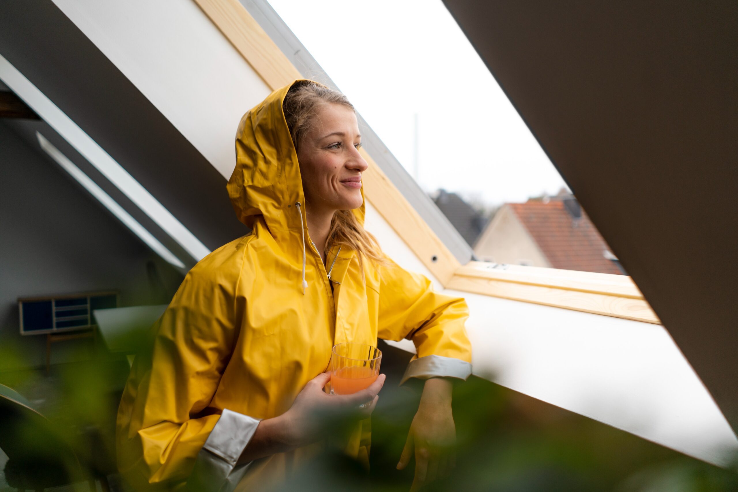A smiling woman wearing a raincoat looks out a window in a hotel while traveling