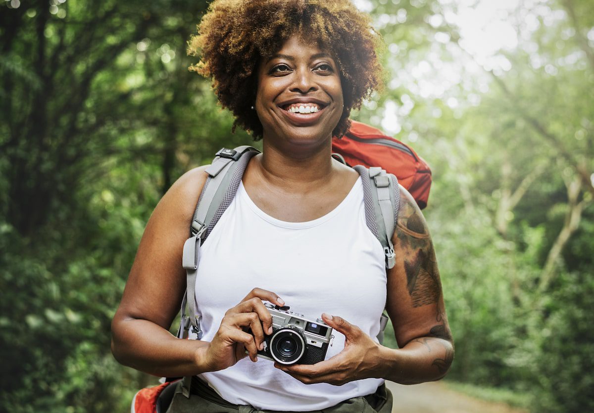 A woman hikes through the woods on an adventure travel trip, holding her camera