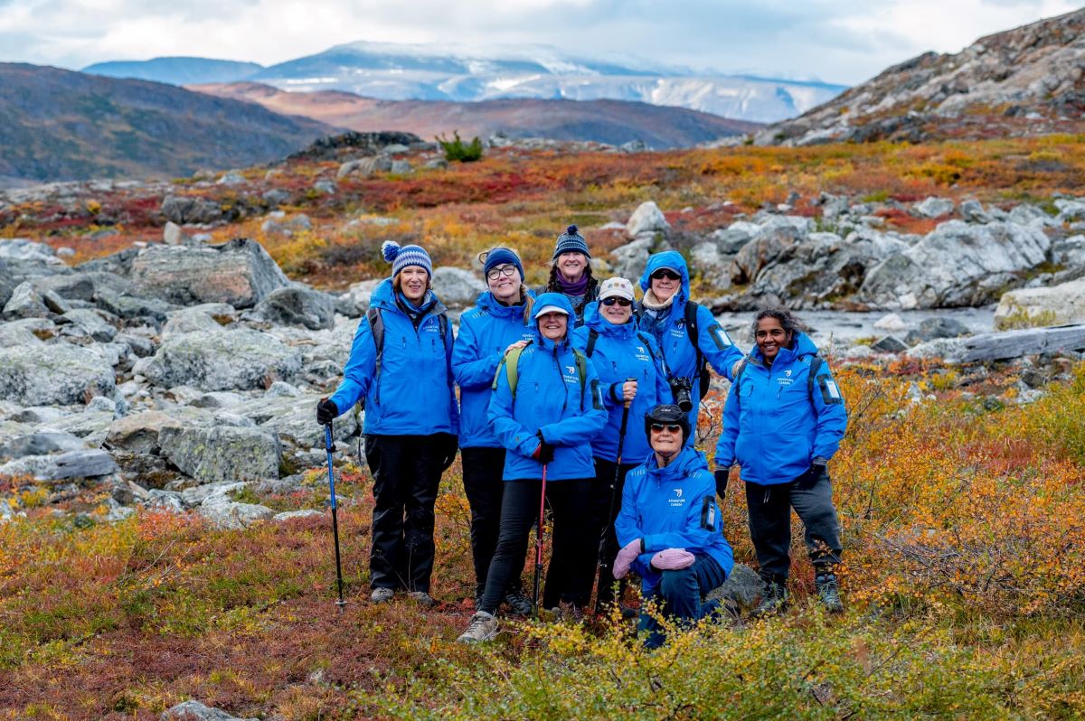 a group of women wearing blue jackets smiling on a mountainside range