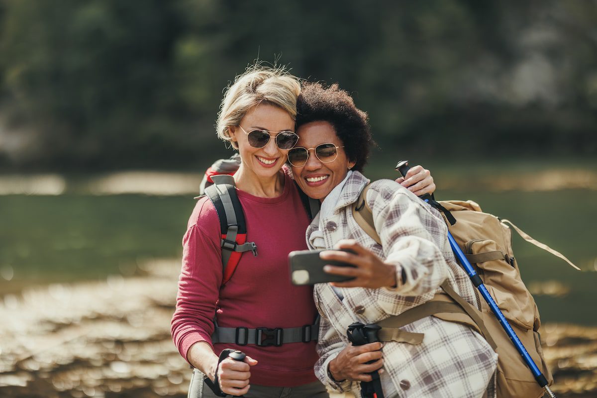 Two women stop to take a photo while on a hiking trip. Traveling more sustainably is one way women can make a difference in travel.
