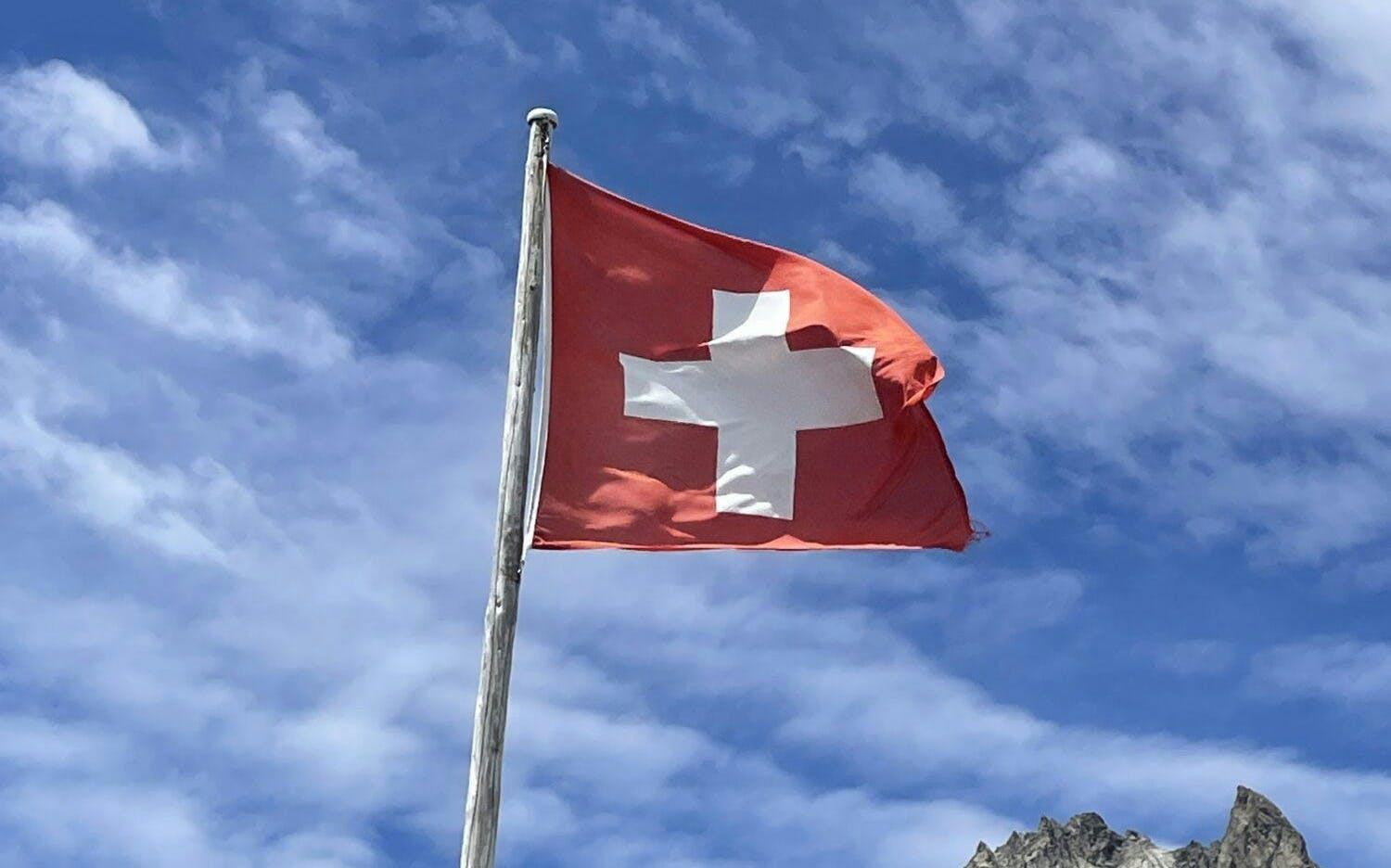 A flag of Switzerland blowing in the wind against a blue sky