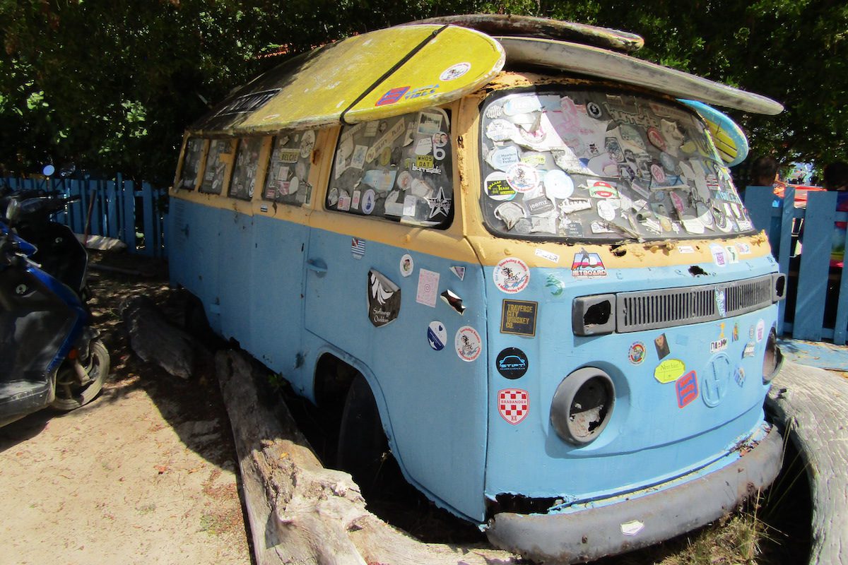 A vintage VW van with surf boards strapped on top on a beach in Bonaire