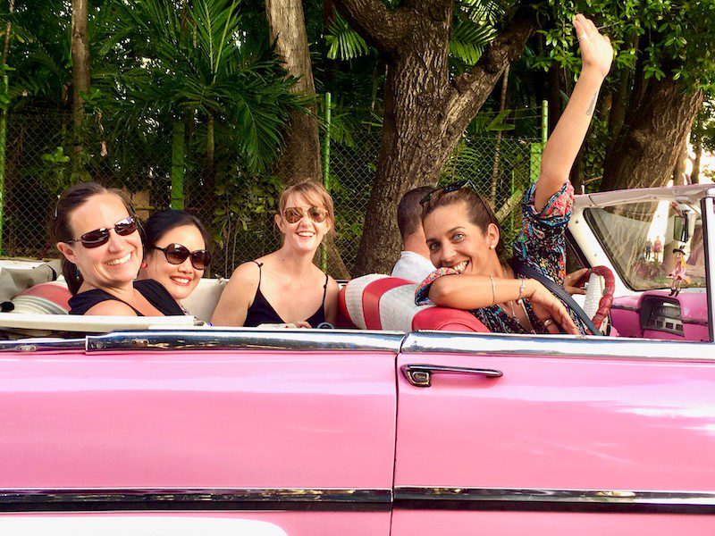 A group of women in a pink vintage car in Cuba