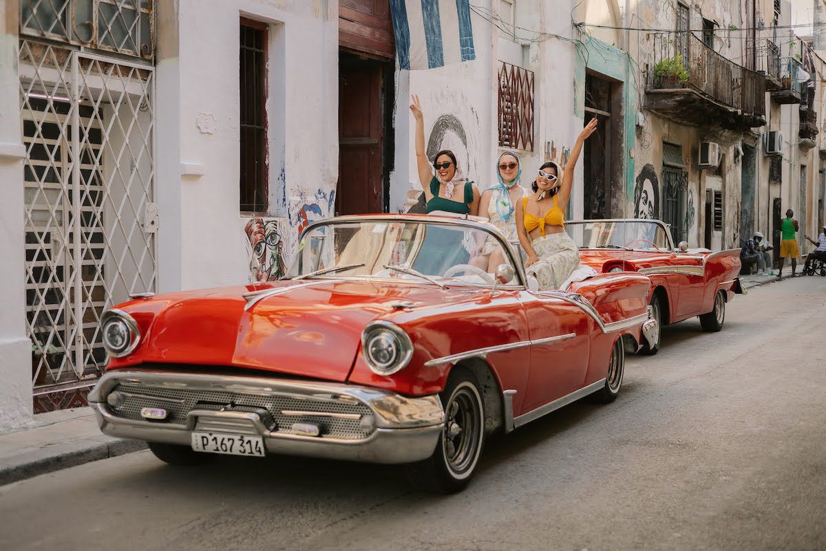 Three women sit in a vintage red car on a tour with Cuban Adventures