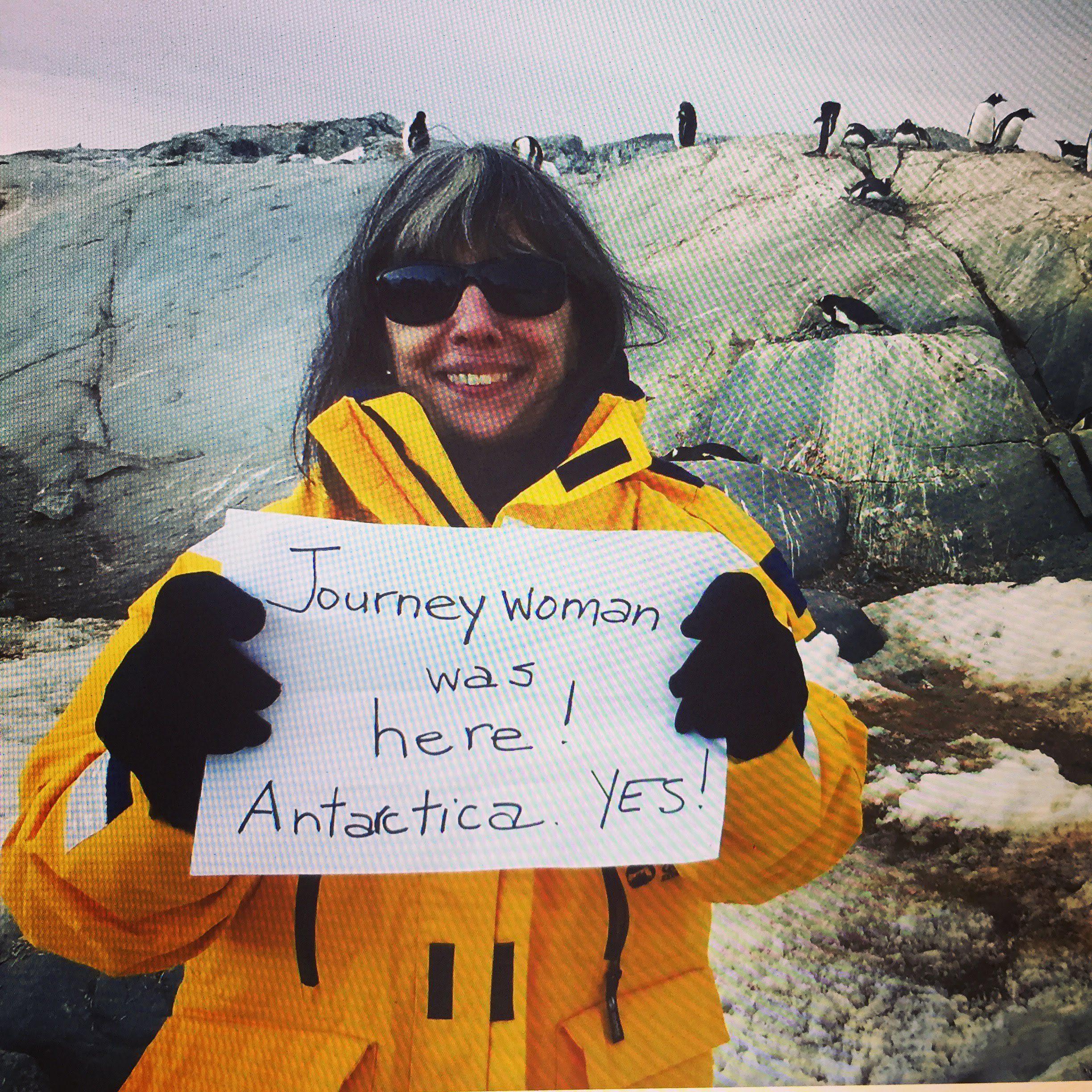 international women's day 2024 celebrating women over 50 with a Evelyn Hannon Journeywoman founder holding a sign in Antarctica