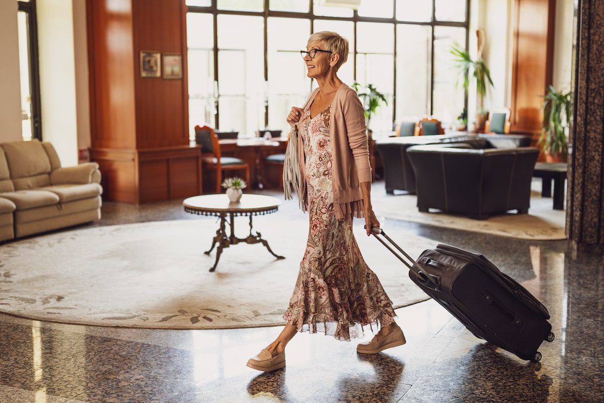 A woman walks through the lobby at an upscale hotel with her luggage.