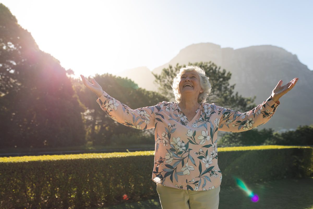Happy senior woman with arms outstretched in sunny garden