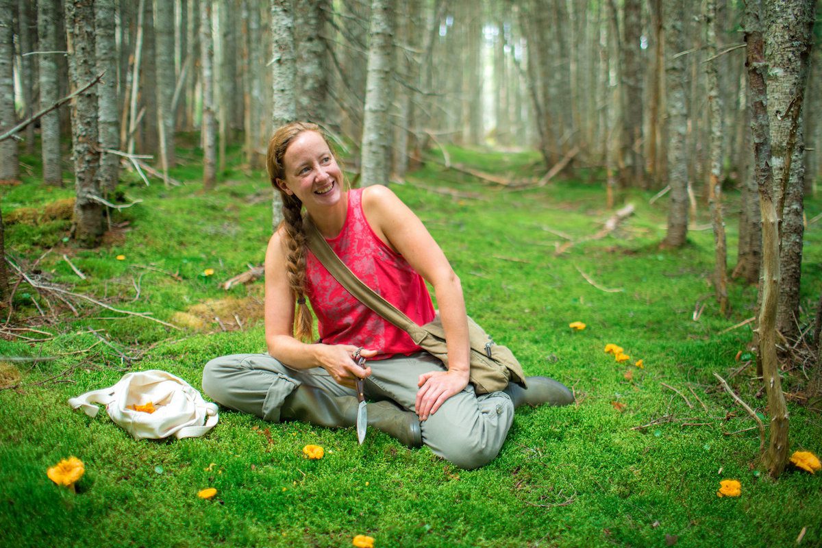 A woman sits on the grass in the middle of the forest.