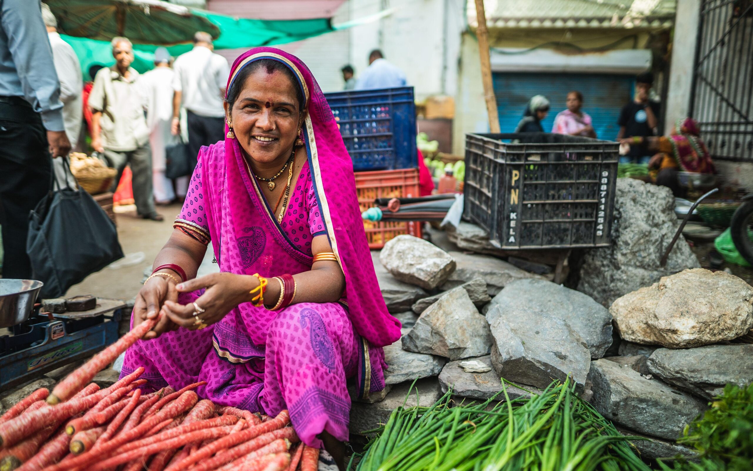 Indian woman wearing a pink sari smiling and sitting down cooking in a local market