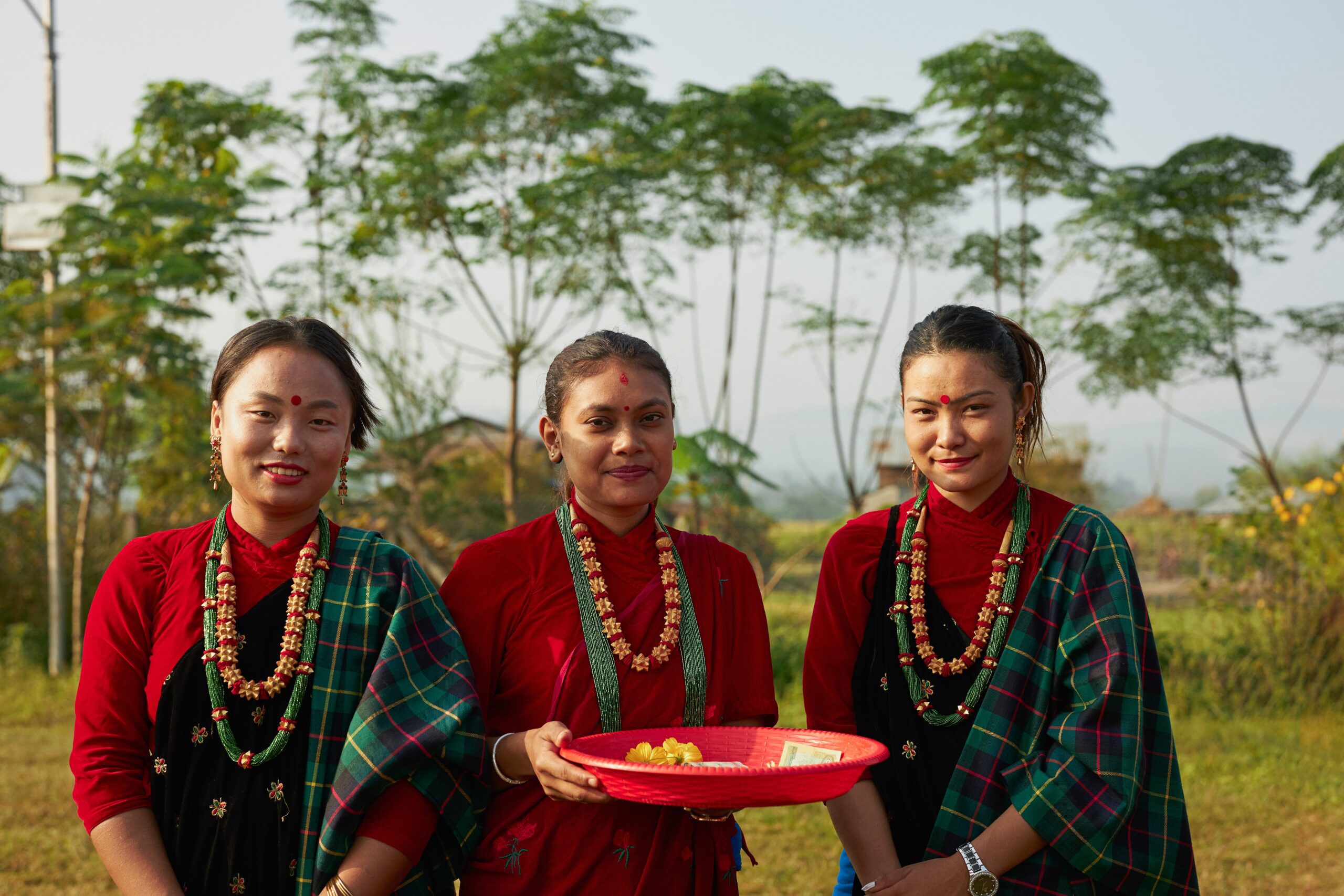 three nepalise women standing next to each other outside dressed in traditional nepalise attire. 