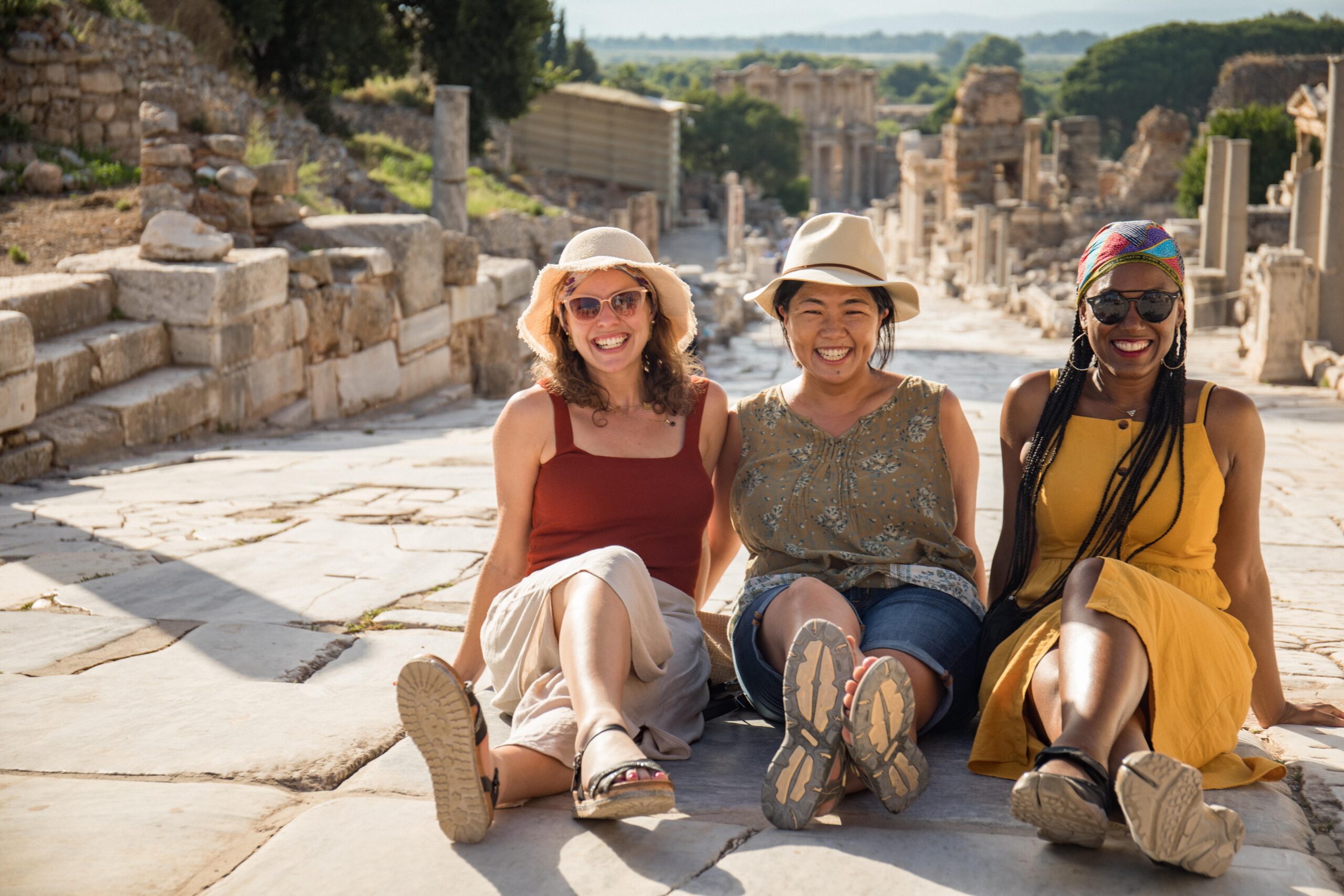 three women sitting down in an open air ruin site. Three women smiling towards the camera