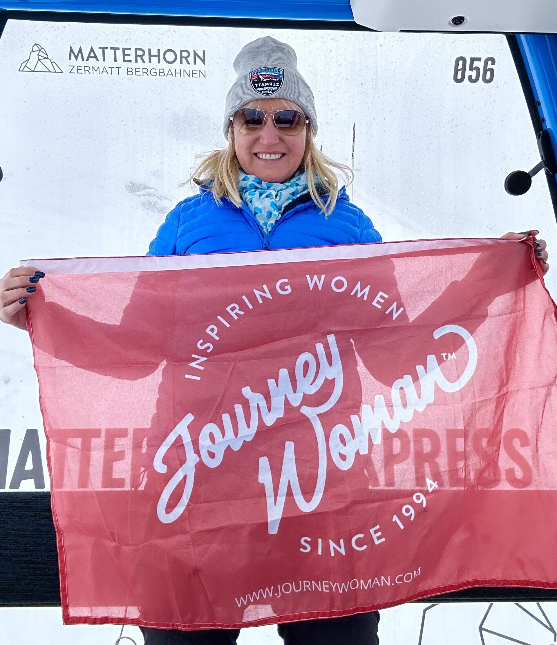 Carolyn Ray holds a JourneyWoman flag while riding a gondola in Switzerland on a Trafalgar Tour