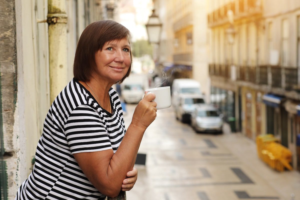 woman holds cup of coffee or tea, standing on the balcony with Europe city street view in the morning