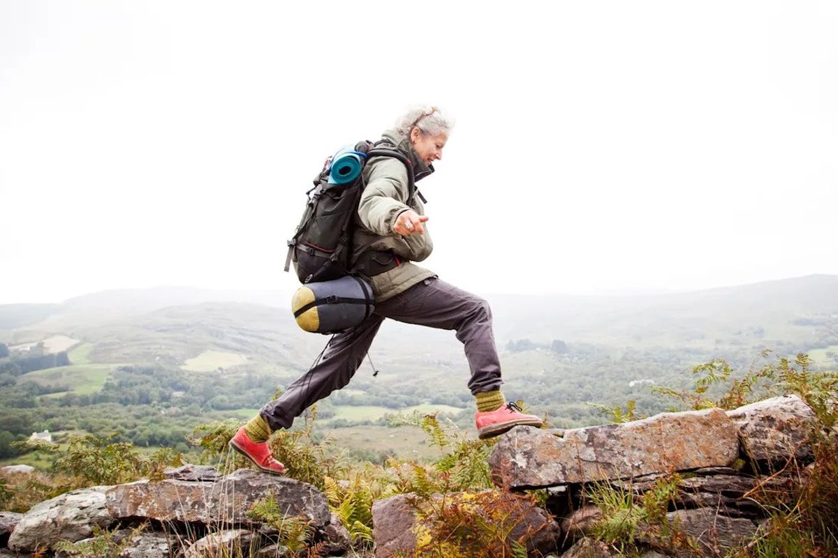 A woman hiking over rocks wearing red hiking shoes.