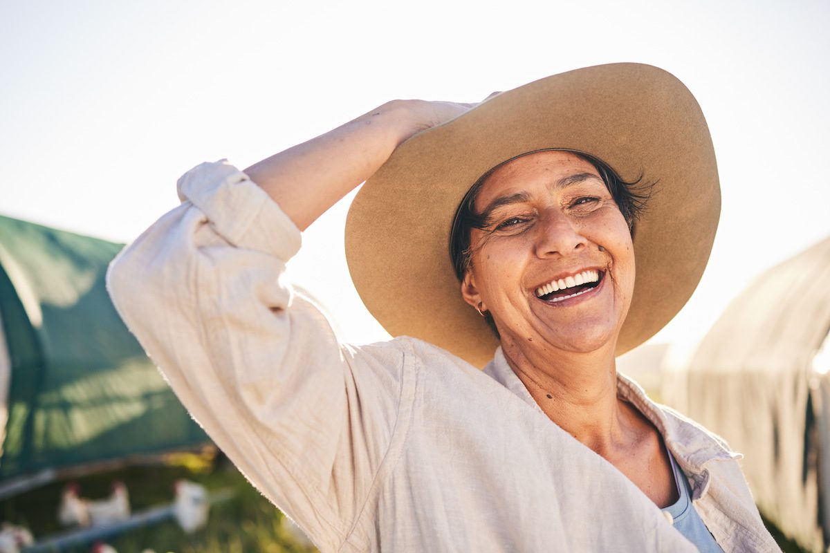 An older woman wearing a sun hat smiling outdoors.