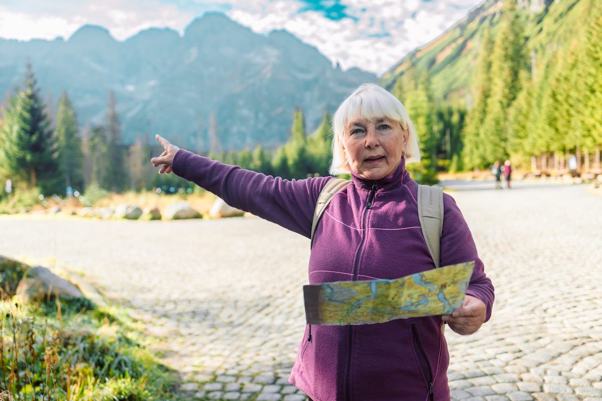 Senior woman traveler with beige backpack with a paper map stands in a Tatra National Park, Poland