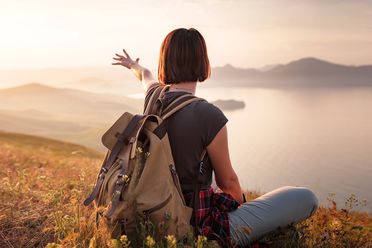 A woman with a backpack Sitting on a hill slope and enjoying the view of the sunset sea and mountains.