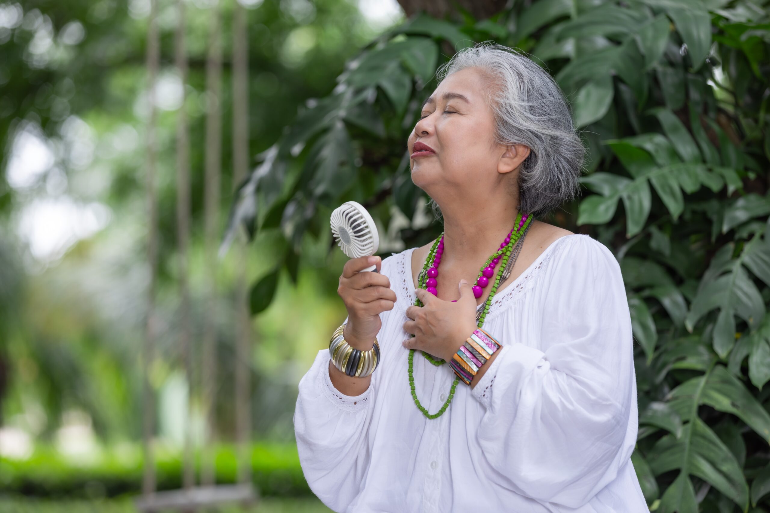 Elderly Woman with Grey Hair Feeling Joyful Outdoors, Holding a Hand Fan menopause