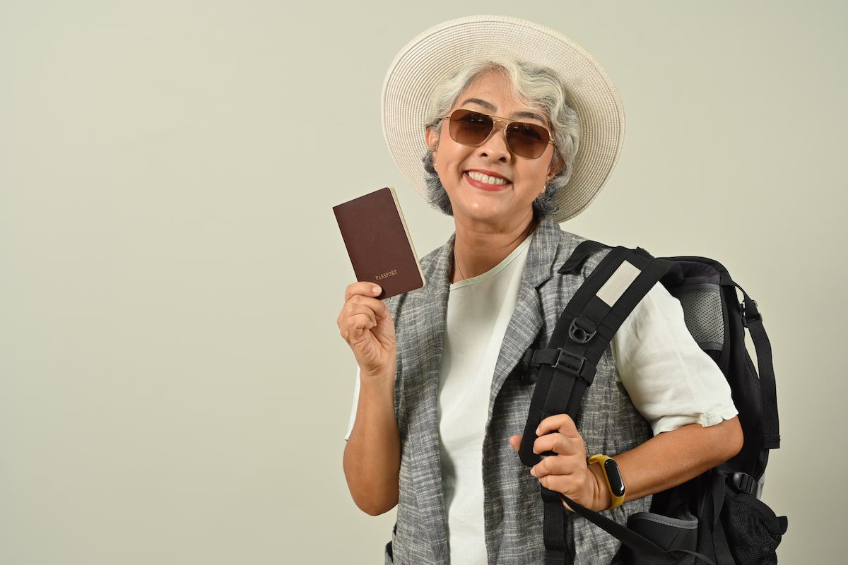 Happy mature woman tourist woman holding passport on gray background