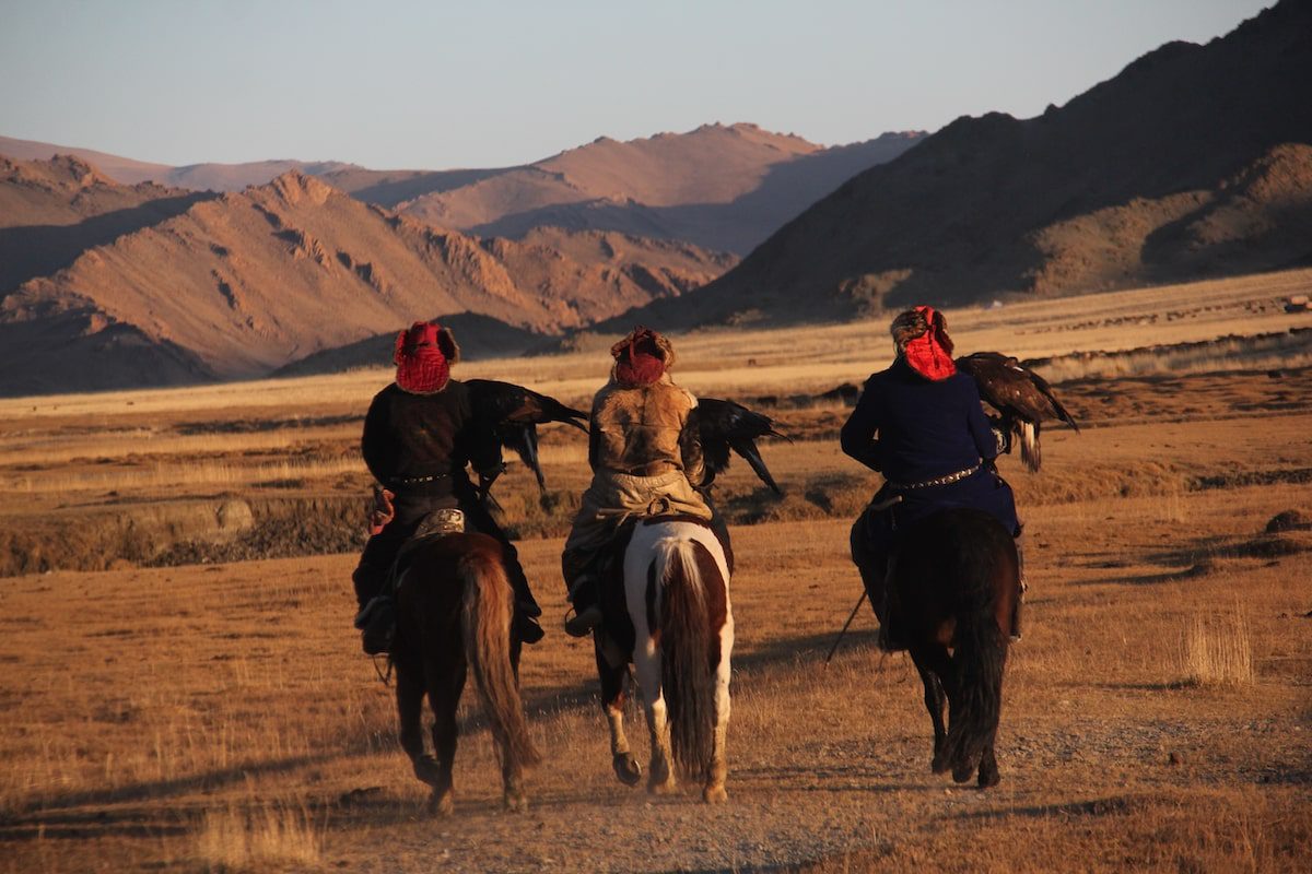 Landscape of a valley with a group of horseriders with birds against a background of mountains in Mongolia