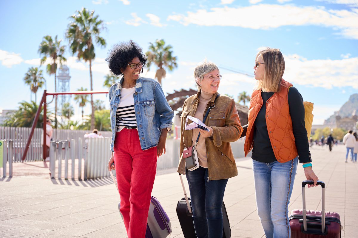 Group mature diverse tourist women walking with luggage while talking and looking at each other