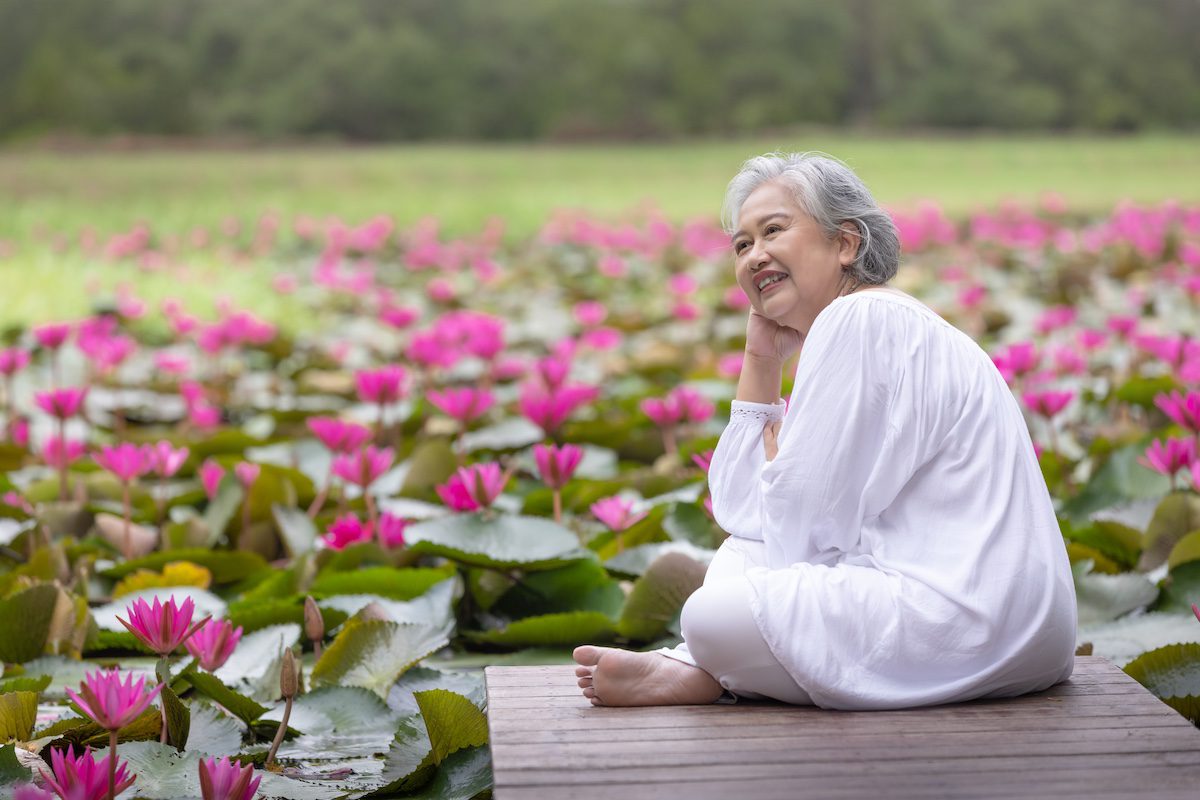 Elderly woman sitting amongst pink water lilies, embracing nature and reflecting on life's tranquility in a serene outdoor setting