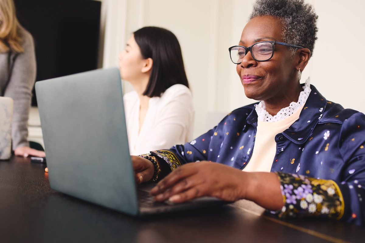 Woman with short gray hair wearing glasses and using laptop