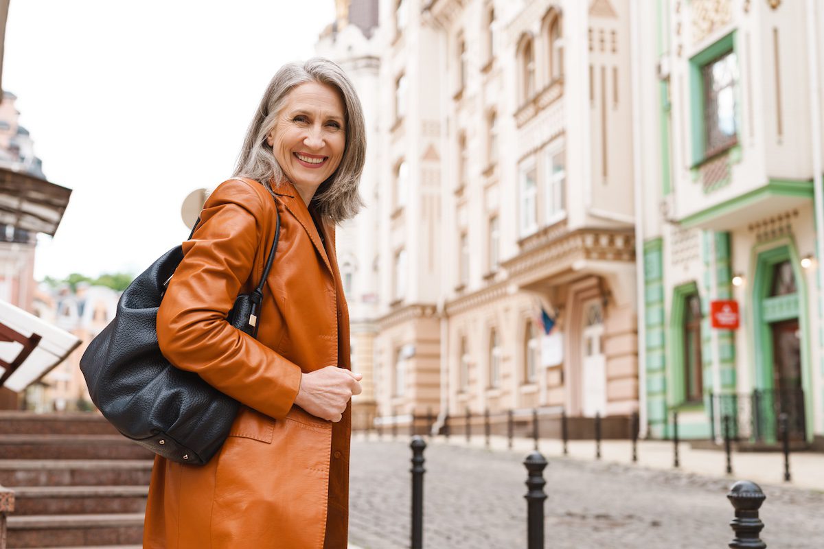 Woman with leather bag smiling while walking on city street