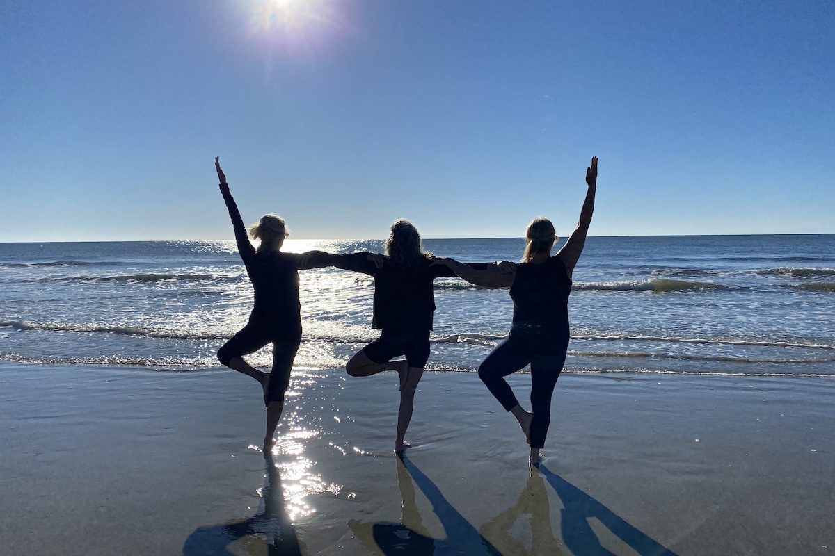 Three women practicing yoga on the beach at Hilton Head wellness retreat