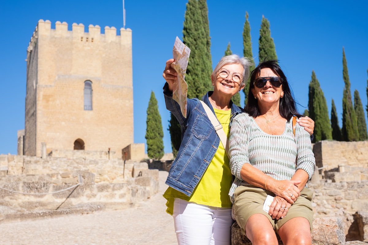 Happy couple of mature senior women visiting a historic castle in Andalusia, Spain, resting looking at landscape.