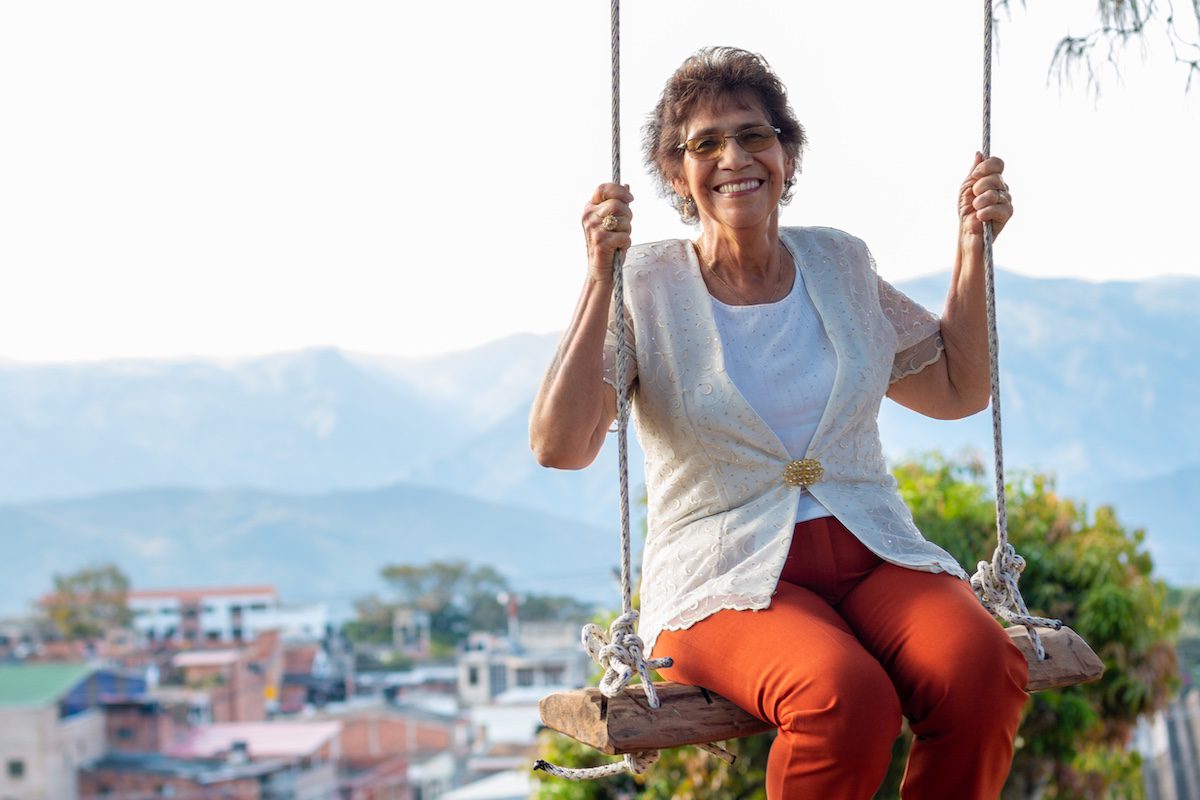 A woman enjoys her retirement and laughs as she plays in nature and swings on a swing.